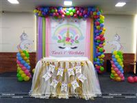Pastel shades of fabric and balloons around a Unicorn banner. Table cover for the Cake table with personalized buntings and two cutouts of Unicorns on either side.